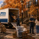 Raimond's Movers foreman reviewing a written moving estimate with customers while the crew loads a truck on an autumn Boston street