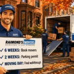 Raimond's Movers foreman holding a fall moving checklist board with 6 weeks book movers, 2 weeks parking permit, and moving day final walkthrough, crew loading a truck on a Boston street