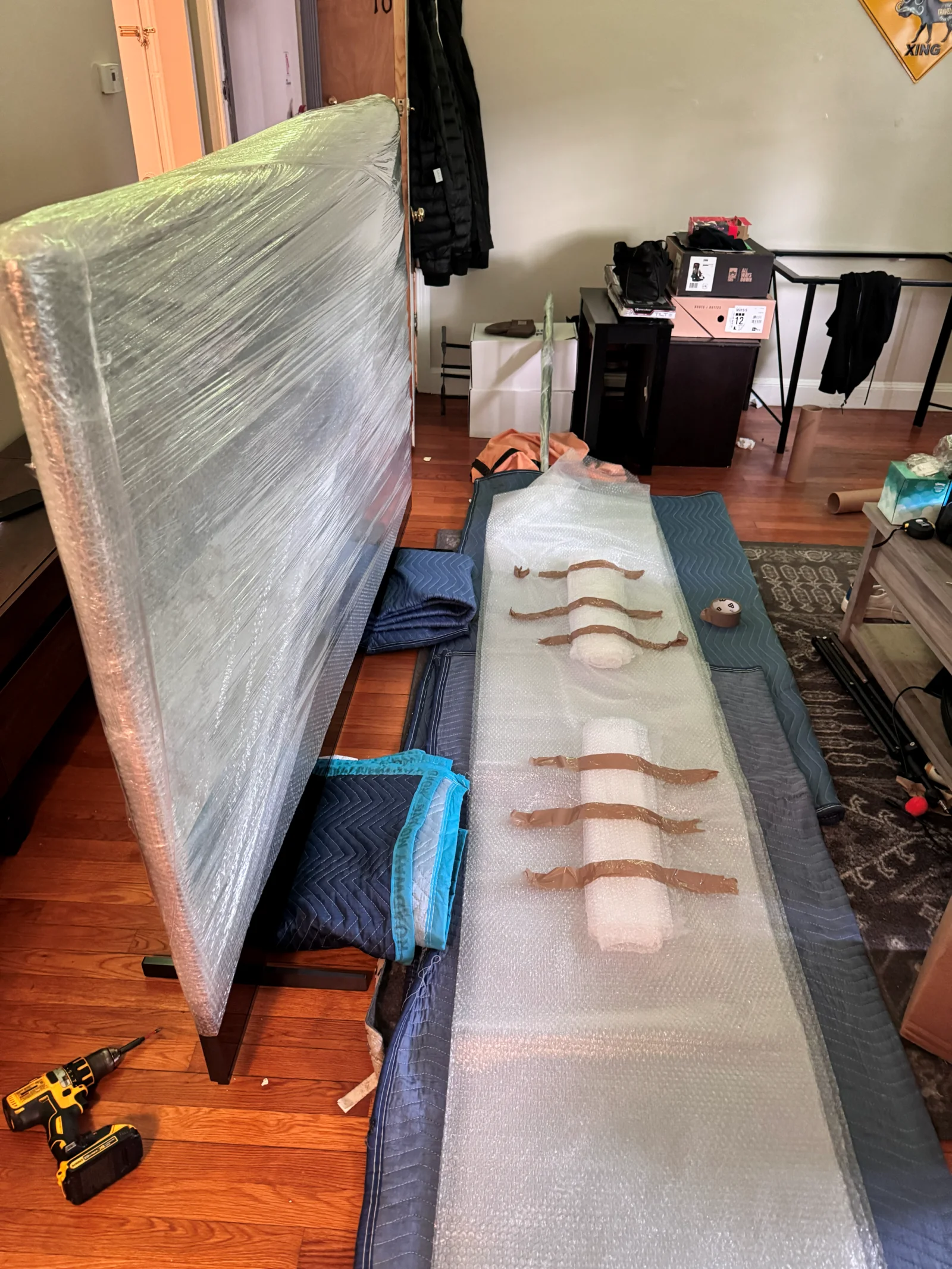 Movers preparing a wrapped mattress and furniture with blankets and packing supplies during a Needham MA move