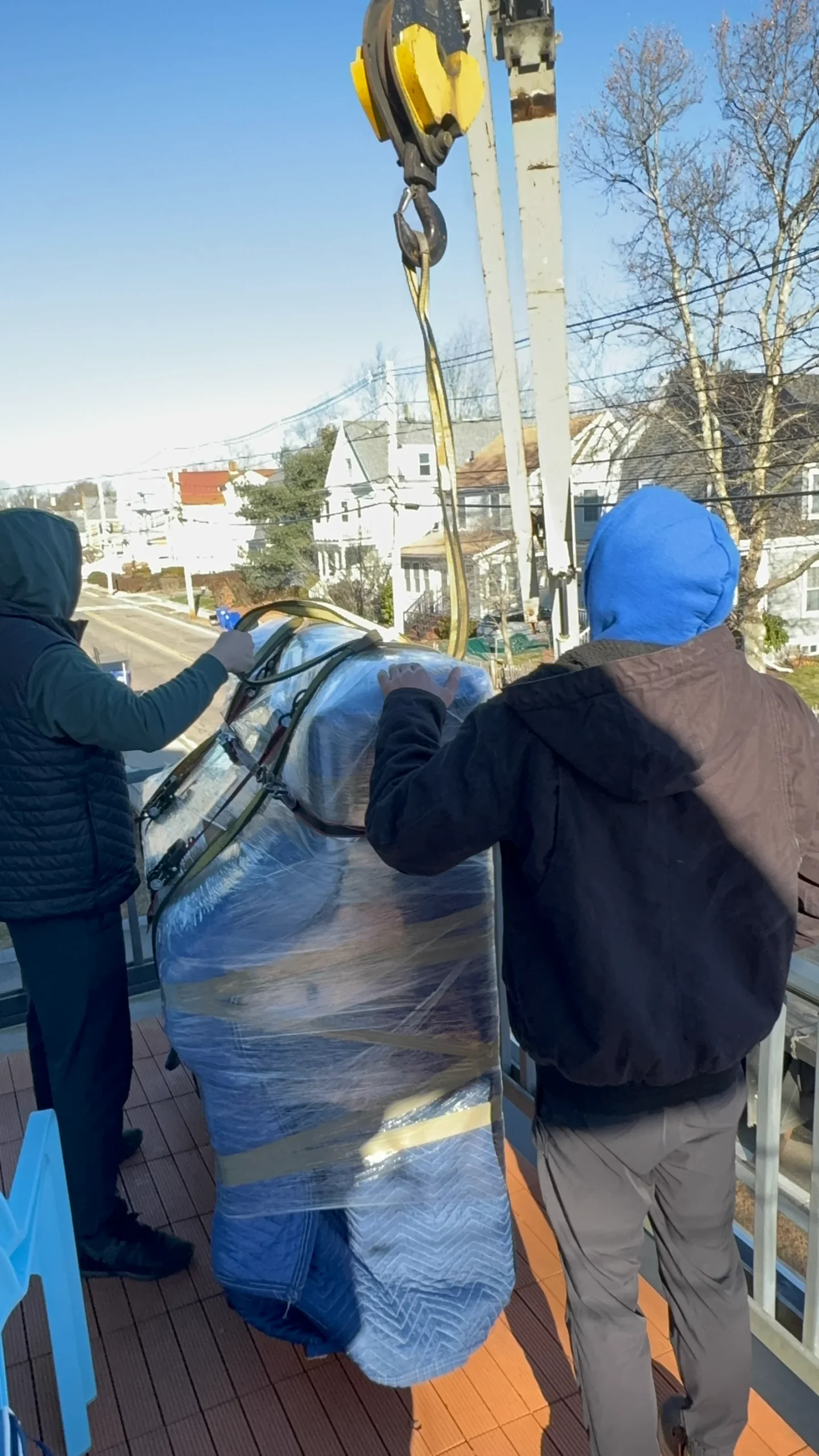 Professional movers using a rigging hoist to lift wrapped furniture from a rooftop deck during a Needham MA move