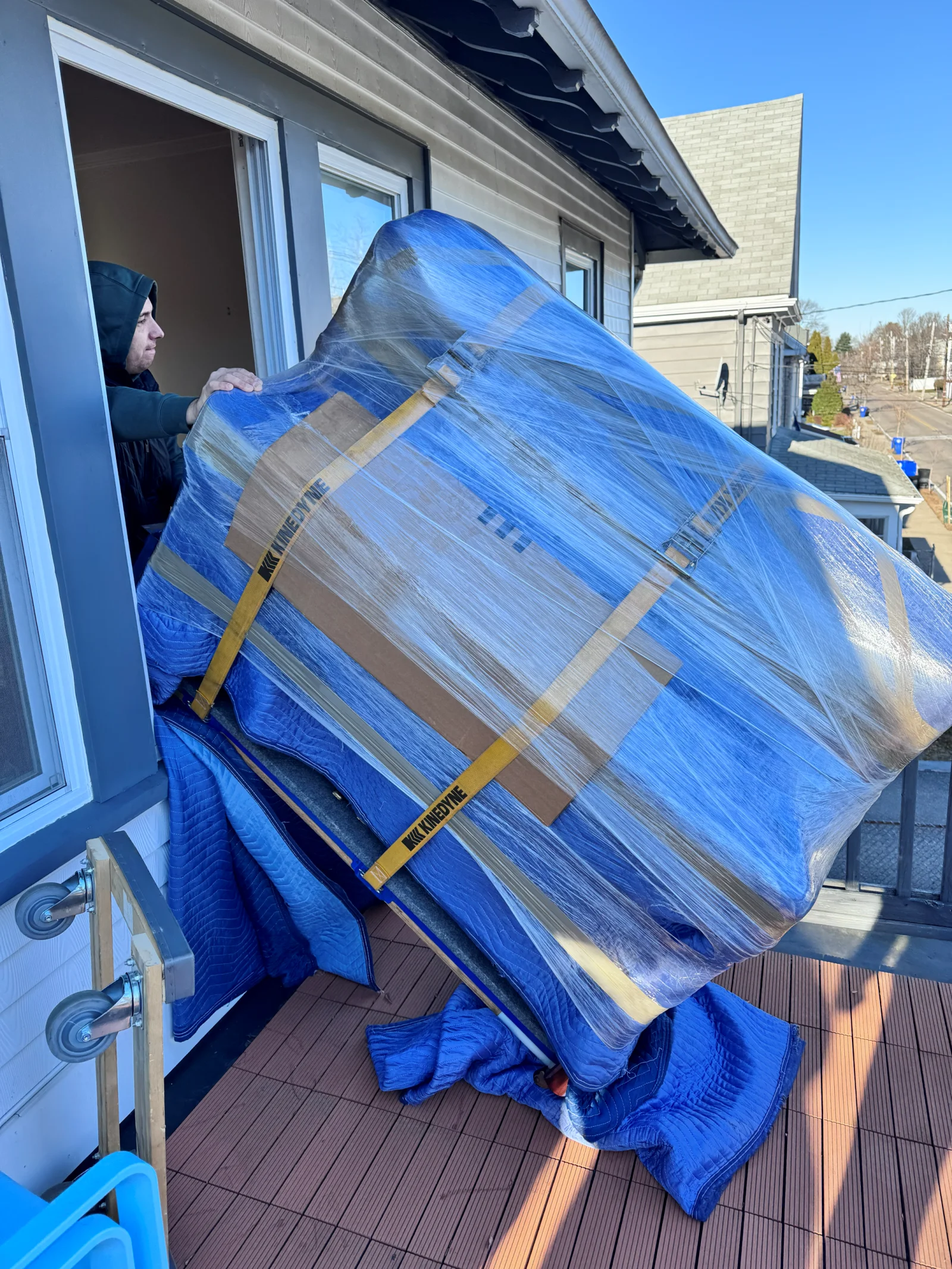 Mover carefully guiding a blanket-wrapped item through a doorway onto a porch during a Needham MA move