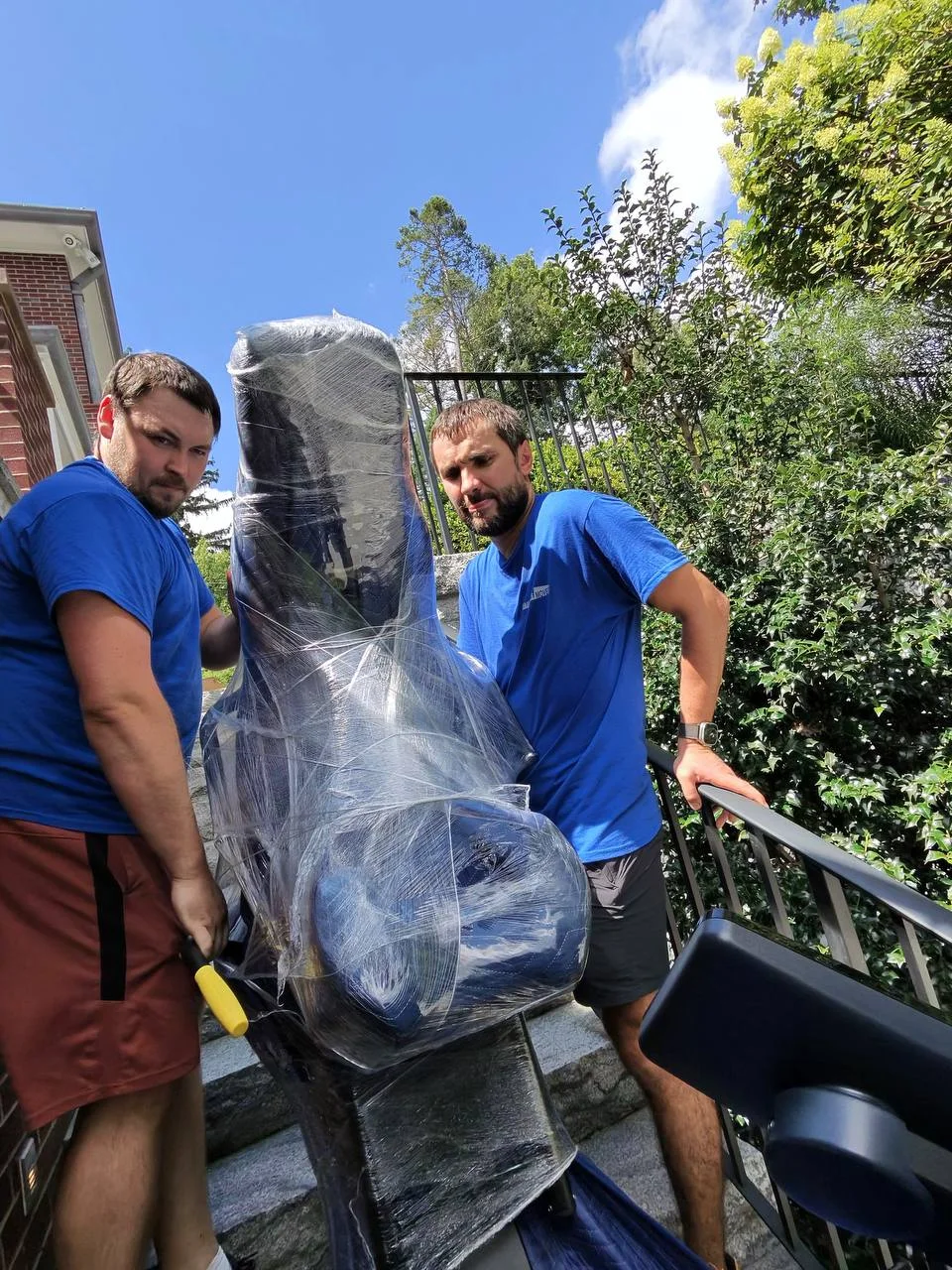 Two Raimond's Movers crew members carefully carrying a wrapped chair down exterior stairs