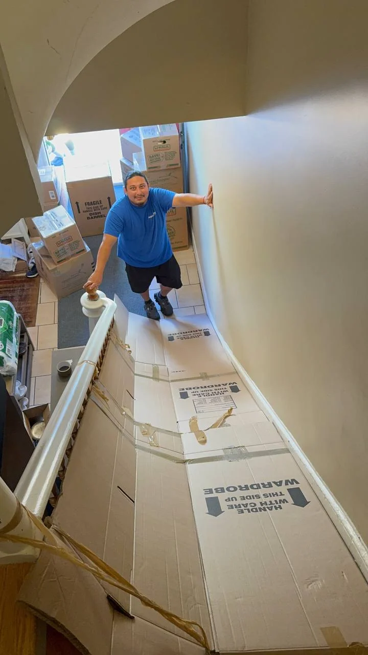 Raimond's Movers crew member carrying labeled wardrobe boxes down a narrow curved staircase, common in older Cambridge buildings